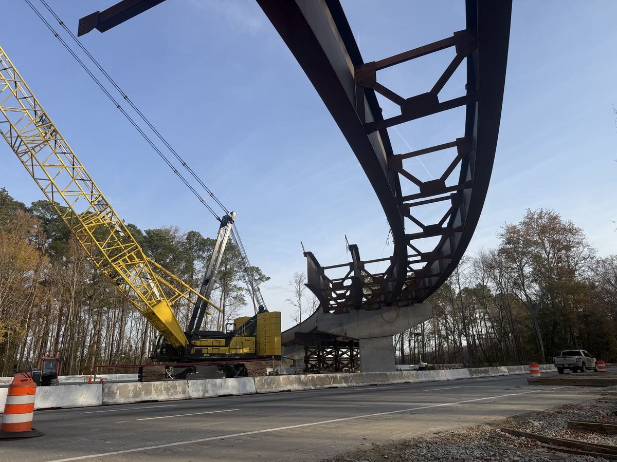 Crane setting a curved steel girder over a highway