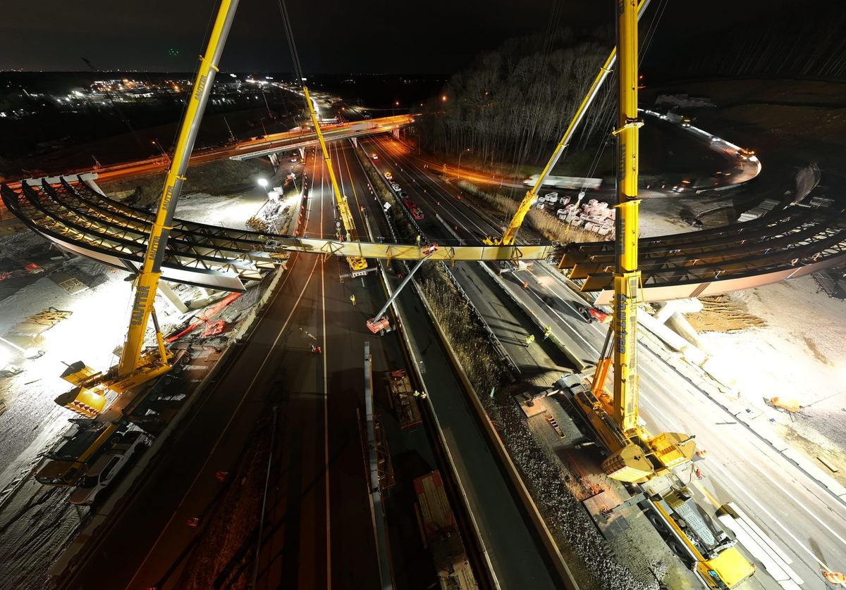 Two cranes setting a curved steel girder span over a highway at night