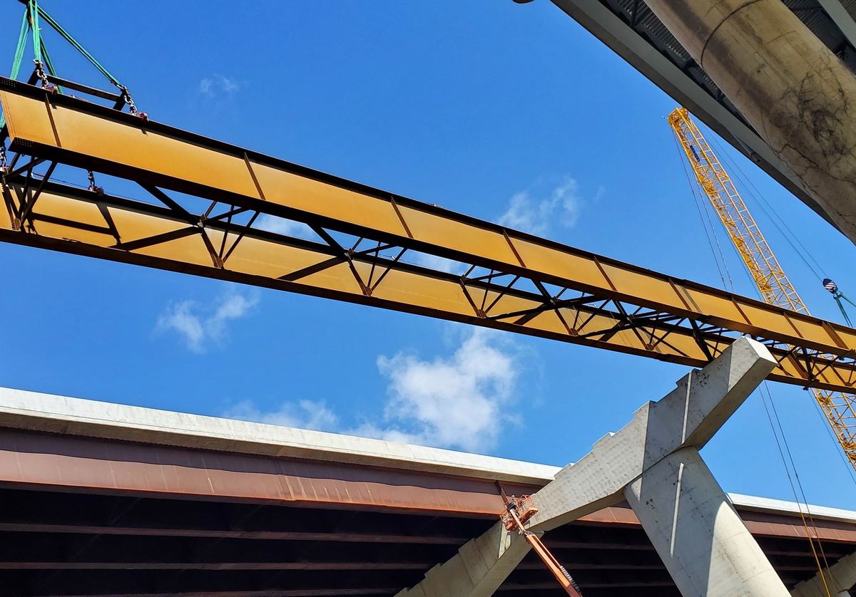 Crane crew setting a steel girder for an elevated transit guideway beside a live highway structure