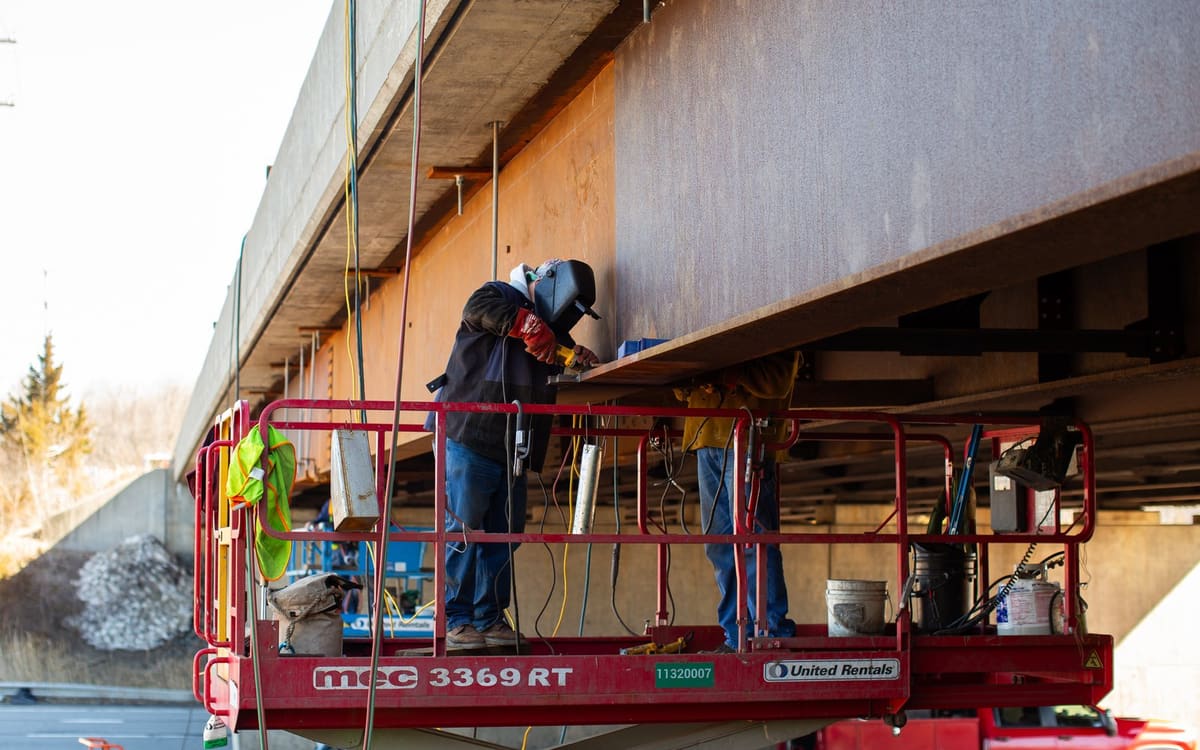 Ironworkers welding on the bottom flange of a bridge girder
