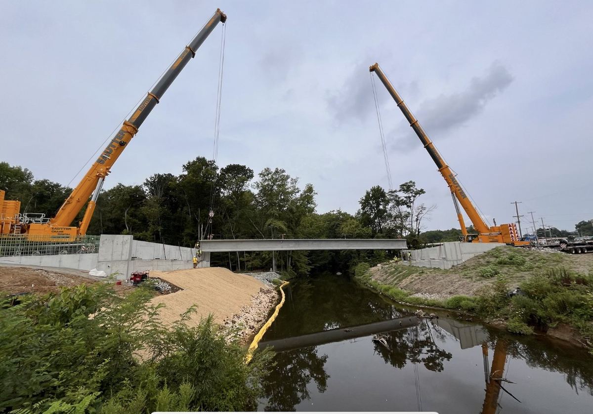 Two cranes setting a precast bridge beam over a creek
