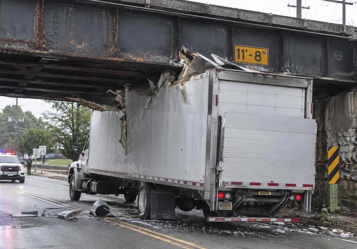 Box truck wedged under a low steel railroad bridge after a strike