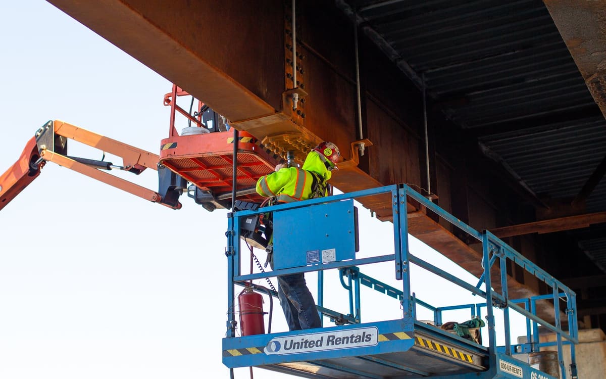 Ironworker working the underside of a bridge girder from a lift