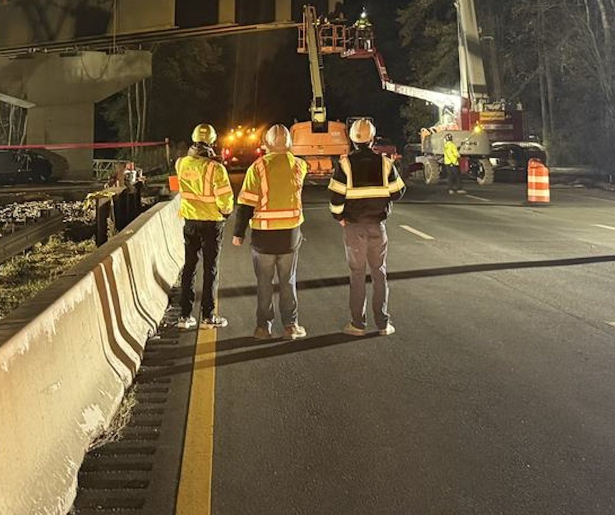 HSE crew watching a night bridge repair from a closed highway lane, aerial lifts working under the girders