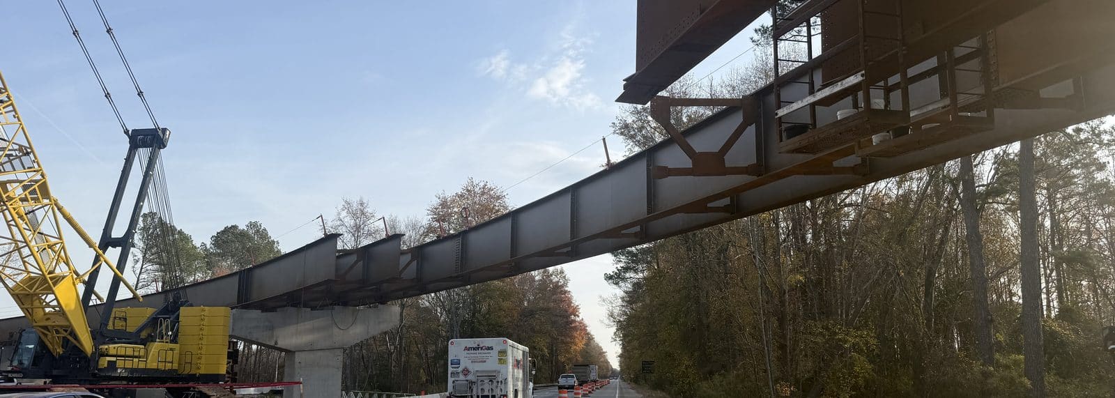 Steel plate girder spanning a highway on falsework, crawler crane alongside and a tractor-trailer passing beneath