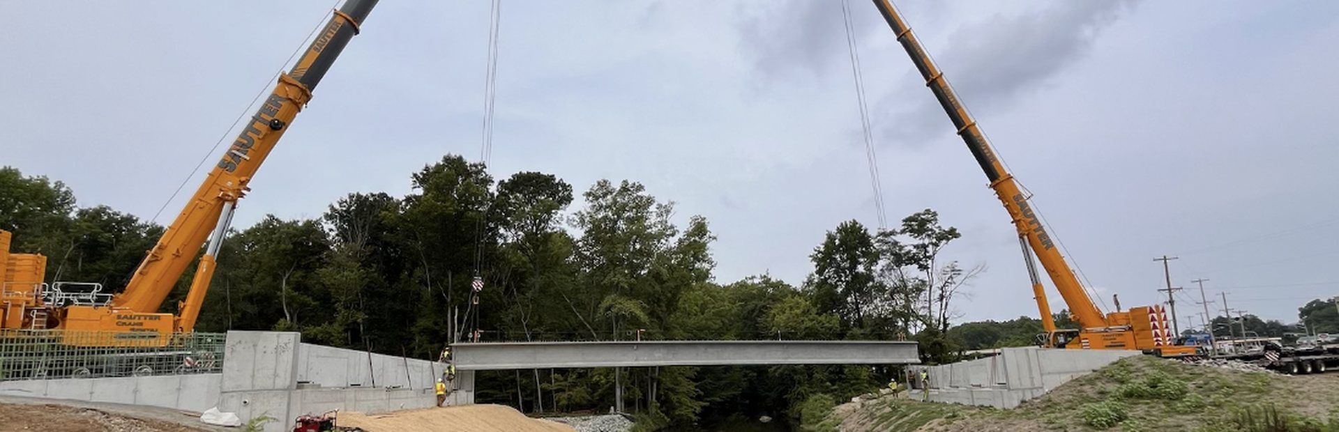 Two cranes setting a precast bridge beam over a creek