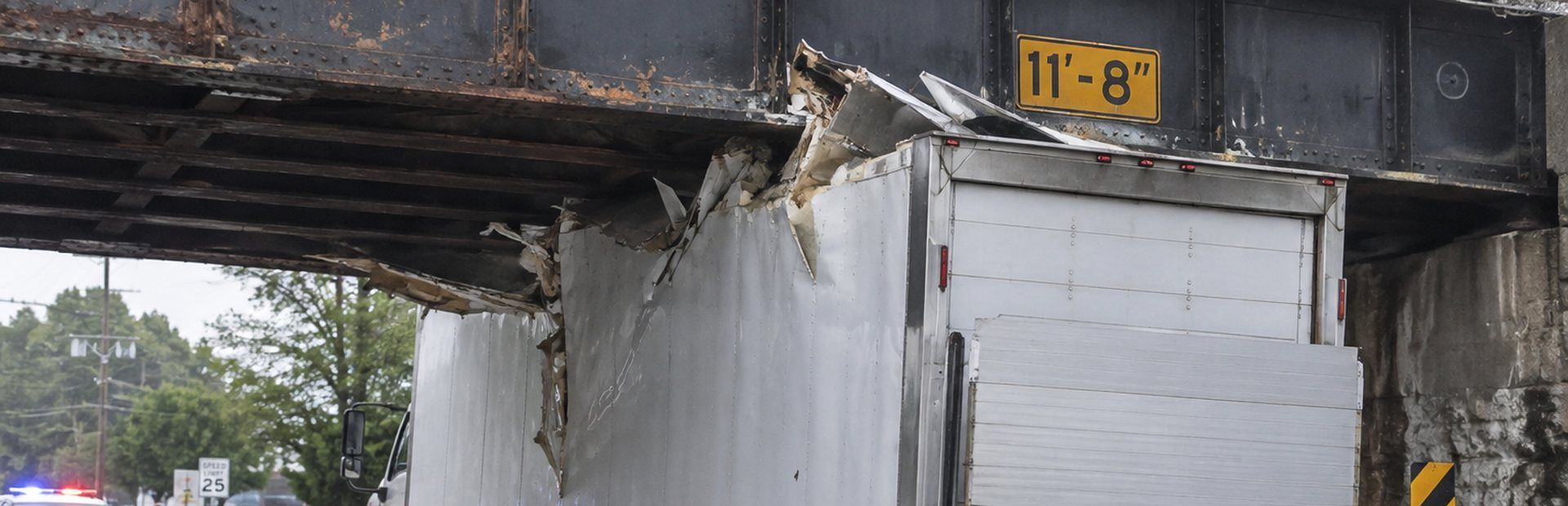 Box truck wedged under a low steel railroad bridge after a strike