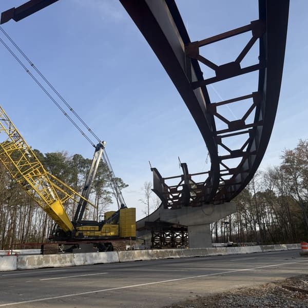 Crane setting a curved steel girder over a highway
