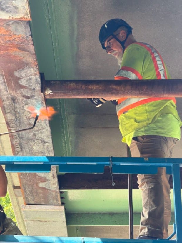 HSE heat straightening supervisor on a lift beneath a damaged steel girder in Westchester County, New York